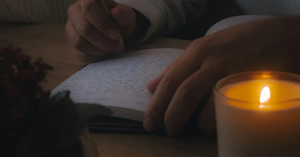 Persona escribiendo en un cuaderno junto a una vela encendida